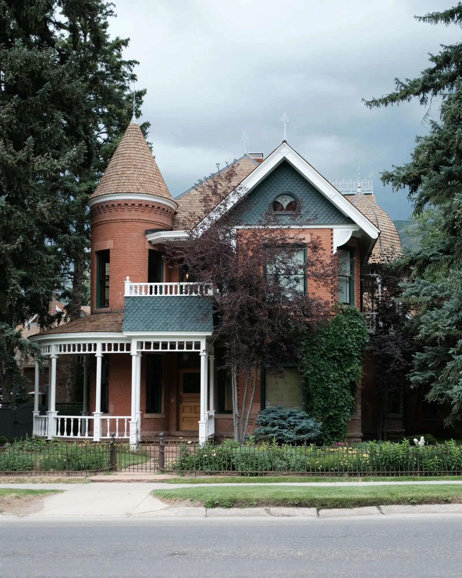 Red brick Victorian with a round turret and a white wraparound porch in Aspen
